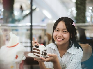 Young Asian teenage girl eating chocolate cake happily. Concept of teenage health and nutrition.