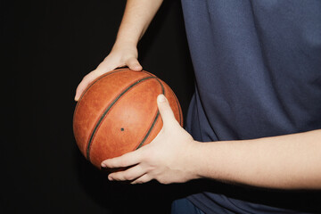 The hands of a basketball player hold the ball to the side, shielding the ball in basketball, individual technique of shielding the ball in basketball on a black background, close-u