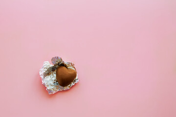 A single milk chocolate candy in an unwrapped wrapper lies on a pink background, the last candy, an...
