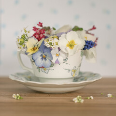 Spring flower bouquet in coffee cup with flowers on it and light blue covered backdrop