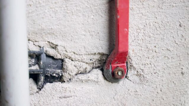 Red metal handle of pipe valve on the wall, cracked wall texture and broken tube inside, repairing plumbing system