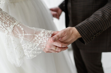 Bride and groom in wedding clothes hold hands with trepidation and love, close-up. Wedding...