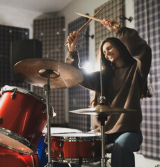 Fototapeta na wymiar Energetic Female Drummer Enjoys Playing Red Drum Kit in a Casual Setting