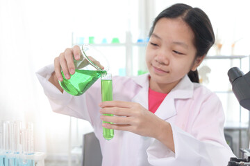 Cute young scientist schoolgirl in lab coat doing science experiments in laboratory.  Student girl child pouring green reagent solution from beaker into test tube. Kid learning science education. - Powered by Adobe