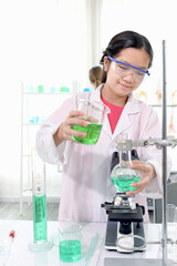 Cute young scientist schoolgirl wearing lab coat and safety glasses, doing science experiments. Student girl child using lab equipment to study chemistry in laboratory. Kid learning science education.