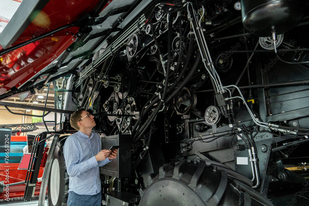 Poster Serviceman with digital tablet on a next to ombine harvester with open hood..