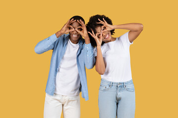 Playful African American couple making funny faces with fingers imitating glasses