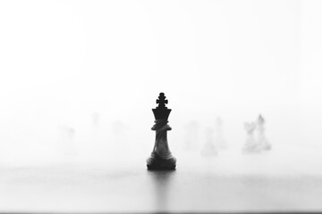 Close up of chessmen on chessboard, with the focus on the centrally placed black king, smoke and...