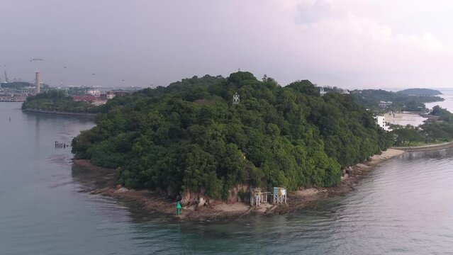 Drone of a rocky beach with a cliff covered by trees along Sentosa Island in Singapore