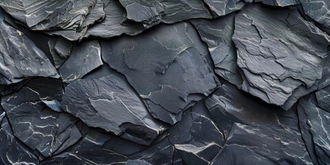 A close up of a rock wall with many different sized rocks. The rocks are all black and the wall is very rough. Scene is one of ruggedness and strength