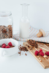 a golden spoon with granola on a wooden board, next to a bowl with raspberries and almonds. in the...