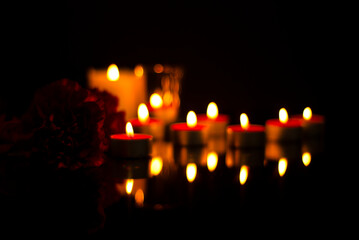 Sad mourning blurred background of burning candles, carnation flower In the silence of the darkness...