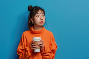 A woman in an orange sweater holding a coffee cup. She is looking at something in the distance