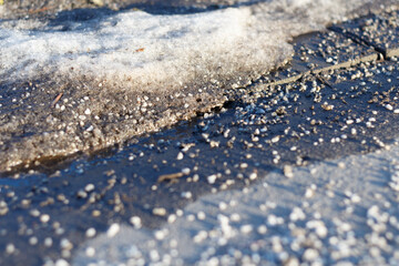 Snow is thawing on the road, the reagent is scattered on the asphalt. Soft focus.