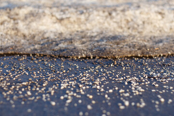 White deicing agent melts ice on the road. Selective focus.