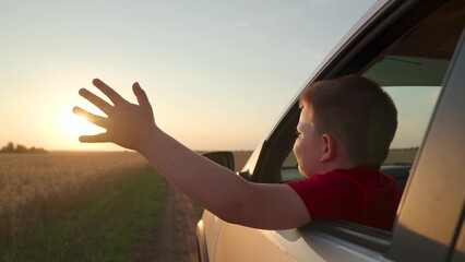 warm sun illuminates fingers, looking out car window while wind gently shakes hair, wind plays hair child bringing feeling freedom, boy son looks out car window admiration, gesture joy, child hand - obrazy, fototapety, plakaty