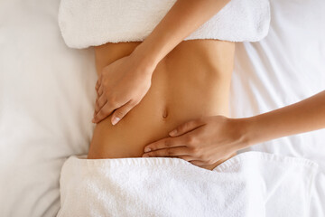 Unrecognizable young woman receiving massage therapy for abdominal area indoor