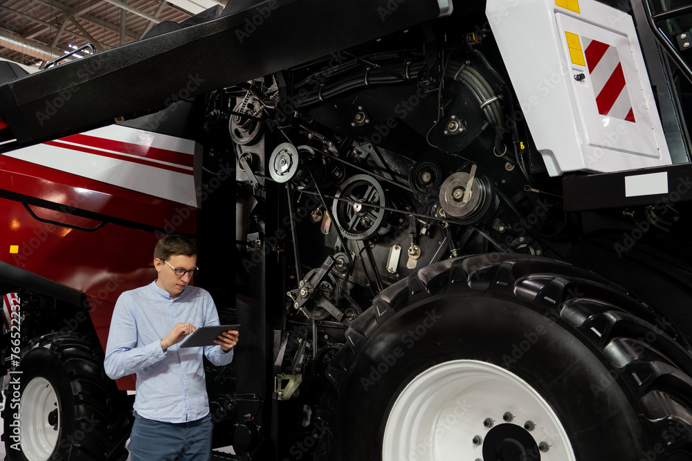 Poster Serviceman with digital tablet on a next to ombine harvester with open hood..