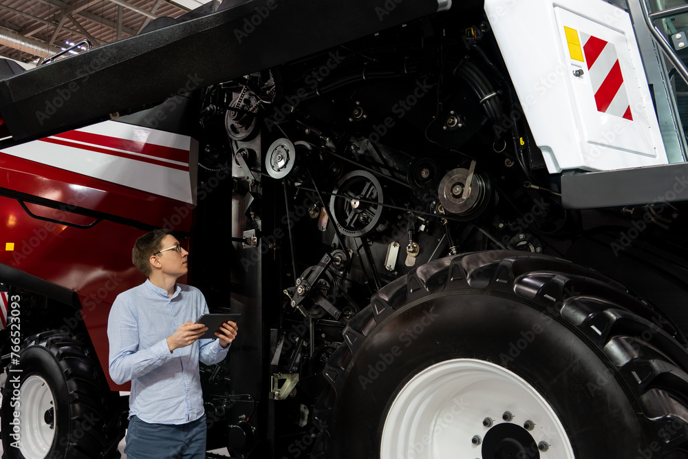 Poster Serviceman with digital tablet on a next to ombine harvester with open hood..