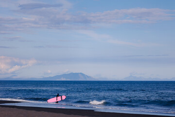 Man with surfboard in wetsuit going to surf in winter ocean Kamchatka Russia