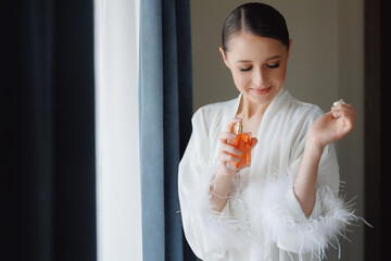 Happy young woman with makeup use perfume, radiant bride smiling. Concept morning and getting ready...