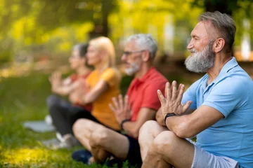 Tuinposter Group of focused seniors practicing yoga in serene park setting © Prostock-studio