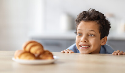 Adorable little boy craving croissant, looking at sweets in kitchen