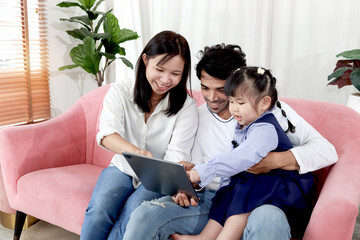 Happy family in living room, Chubby little girl daughter with her mother and father using tablet in living room. Kid spending online together with parents at home. Child, mom and dad in house.