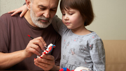 A joint hobby of grandfather and granddaughter. They paint a molded toy made of clay.