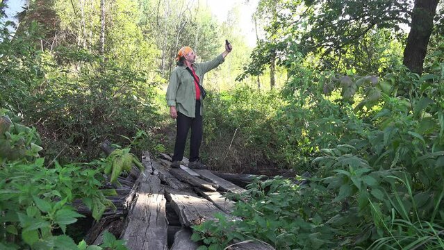 Еraveler, tourist, man in yellow headscarf stands on destroyed old bridge in middle of forest and talks and talks via video connection, blogs