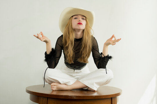 Pretty young woman in white jeans, lacy black top and cowboy poses in a studio setting.