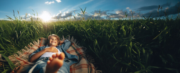 Hintergründe Vorlagen draußen im Freien ein Junge liegt glücklich lächelnd barfuß auf einer Decke im hohen grünen Gras in Sommer Sonne Strahlen genießt Freizeit Urlaub Ferien Natur Freiheit Schönheit  - obrazy, fototapety, plakaty
