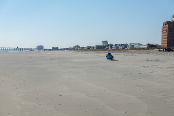 A single person sitting on a beach chair on a wide empty sandy beach