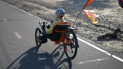 Rear side view of elderly senior woman riding a recumbent electric bike on a bike path in Southern...