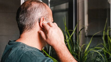 Unrecognizable middle aged man adjusting hearing aid