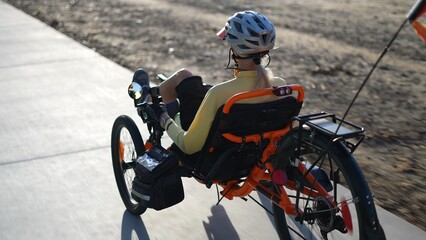 Closeup rear side view of elderly senior woman riding a recumbent electric bike on a bike path in...