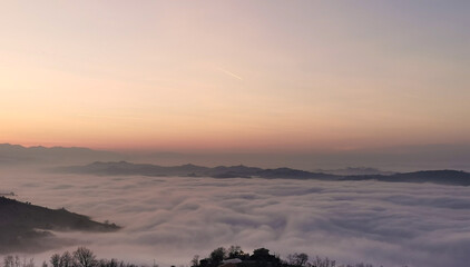 Un mare di nuvole bianche  e di nebbia riempie le valli sotto le montagneal tramonto  - obrazy, fototapety, plakaty