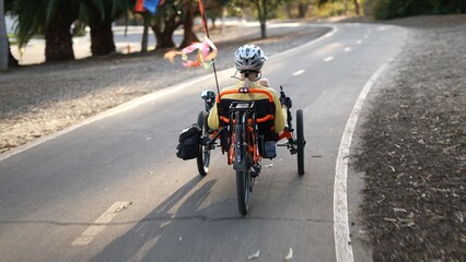 Rear view of elderly senior woman riding a recumbent electric bike on a bike path through a neighborhood in Southern California. Filmed in.