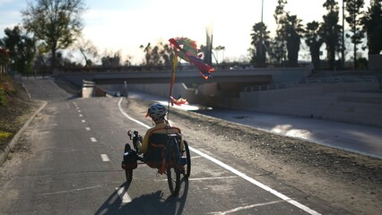 Rear view of mature woman riding a recumbent electric bike on a bike path next to Aliso Creek in Southern California. Filmed in.