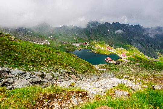 alpine landscape of fagaras mountains. balea lake of romania in summer. cloudy weather in dappled light. spots of snow and grass on the rocky hillsides of carpathian range