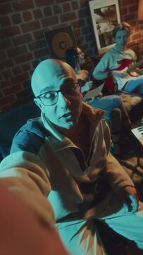 POV UGC vertical footage of male bald blogger in glasses recording his friends singing song to guitar in retro studio and he talking to camera in evening