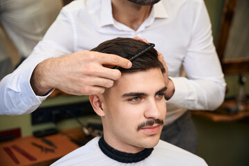 Skilled coiffeur combing client's hair after cutting in barbershop