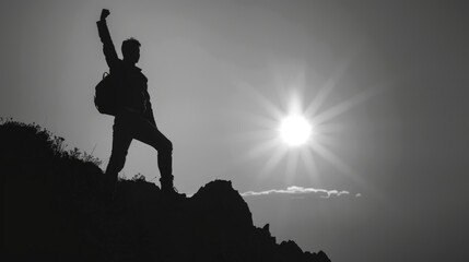A man is standing on a mountain with his arms raised in the air. The sun is shining brightly in the background, creating a sense of accomplishment and triumph