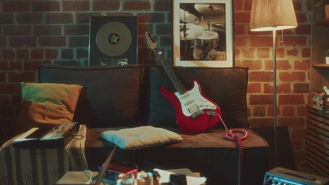 No people handheld footage of anonymous musicians room in retro style with brick walls and red bass guitar, beat maker machine pad and music award on old sofa in eveningNo people handheld footage of a