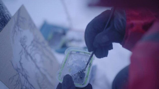 Man Mixing Paint With Paintbrush In Lid By Canvas During Winter - Fairbanks, Alaska