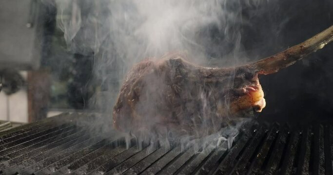 Tomahawk steak grilling on barbecue charcoal grill in smoke. Grilling BBQ meat