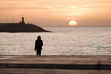 Playa de Málaga, hombre mirando el amanecer, primeros rallos de sol, en el horizonte el sol saliendo desde el mar, vista del faro del puerto de Málaga