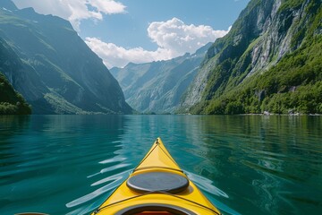 The bow of a yellow kayak slices through the glassy waters of a fjord, mountains soaring into the sky above. - obrazy, fototapety, plakaty