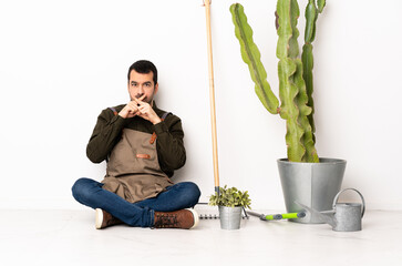 Gardener man sitting on the floor at indoors showing a sign of silence gesture