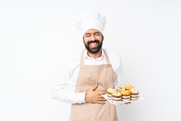Young man holding muffin cake over isolated white background smiling a lot